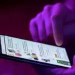 Person views product ads on a smartphone under purple light.