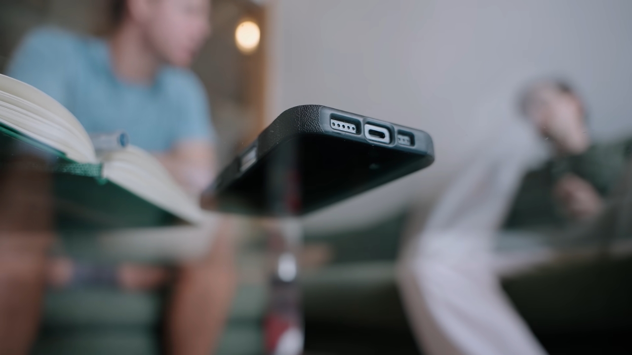 Smartphone rests on a table as two people sit nearby.